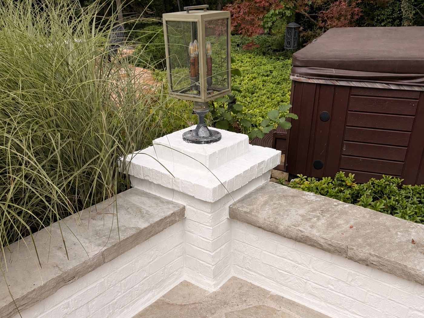 After: the rebuilt brick pillar painted white with a lantern on top, beside stone-capped walls and a flagstone patio