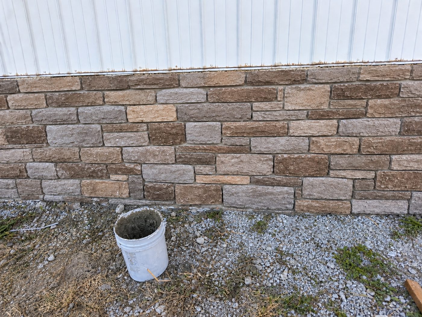 After: the same wall finished with a multicolor stone veneer in tan, brown, and gray tones