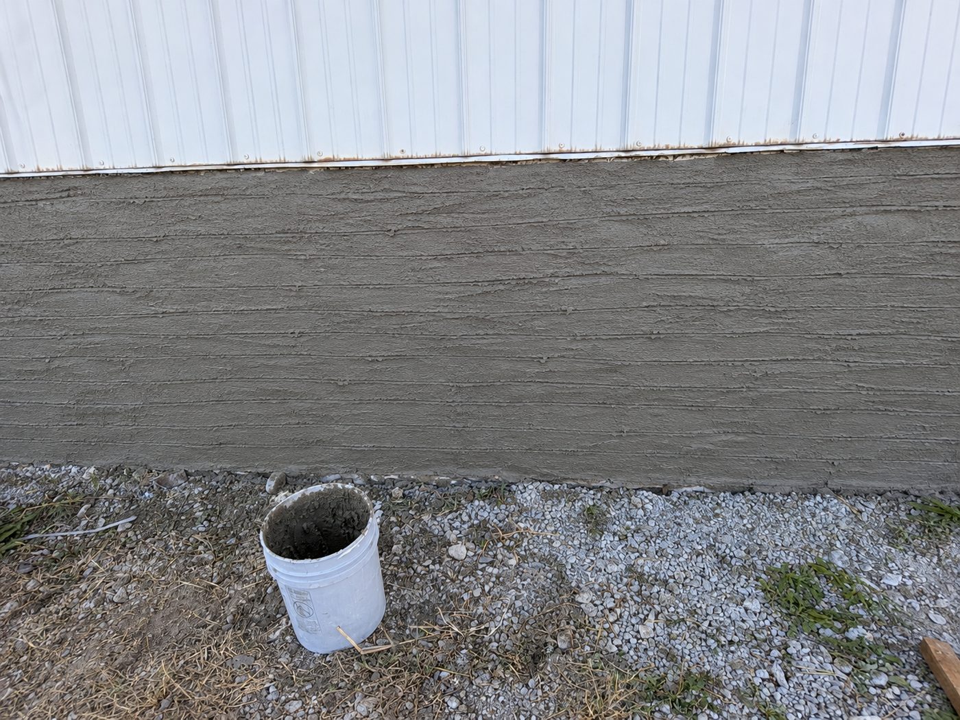 Before: a rough scratch-coated mortar base along the bottom of a white metal building wall