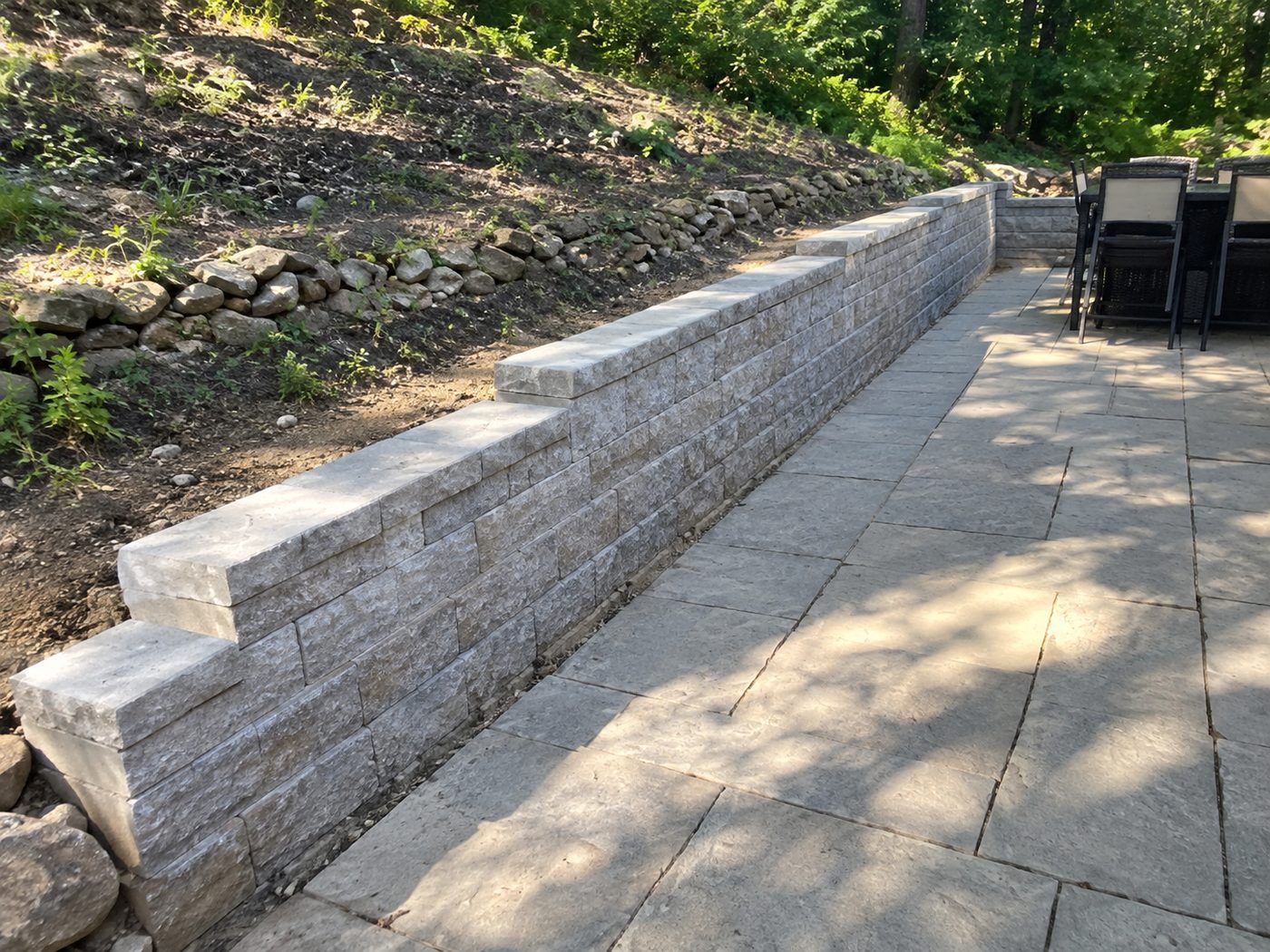 After: a new tiered retaining wall with a cut-stone cap beside the patio, holding back the hillside