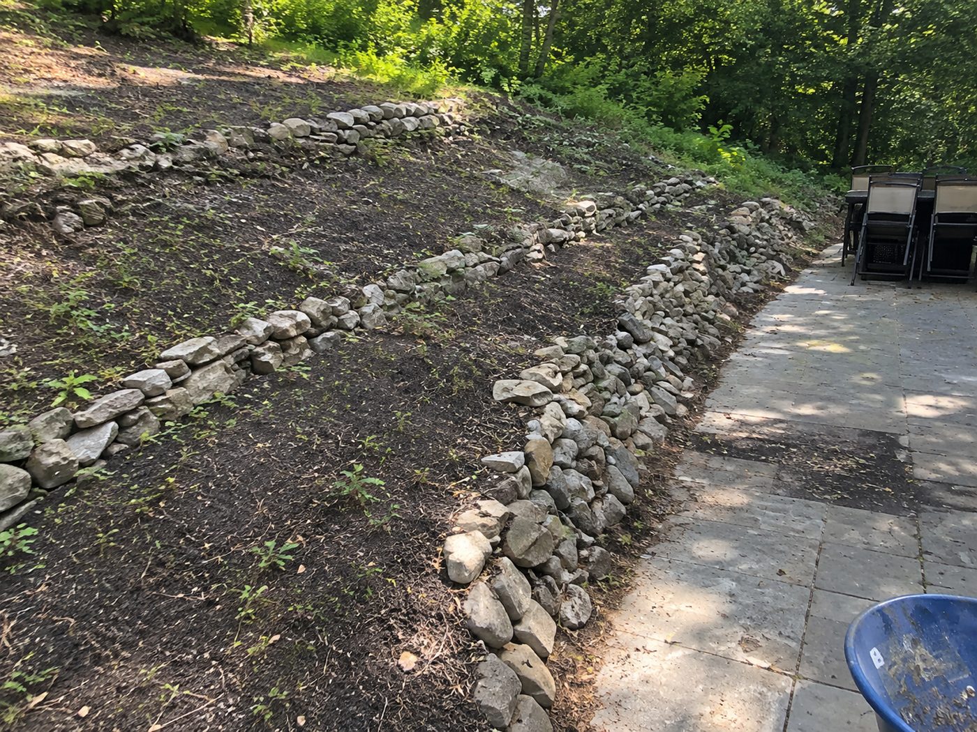 Before: a sloped hillside with loose, stacked fieldstone along the edge of a stone patio