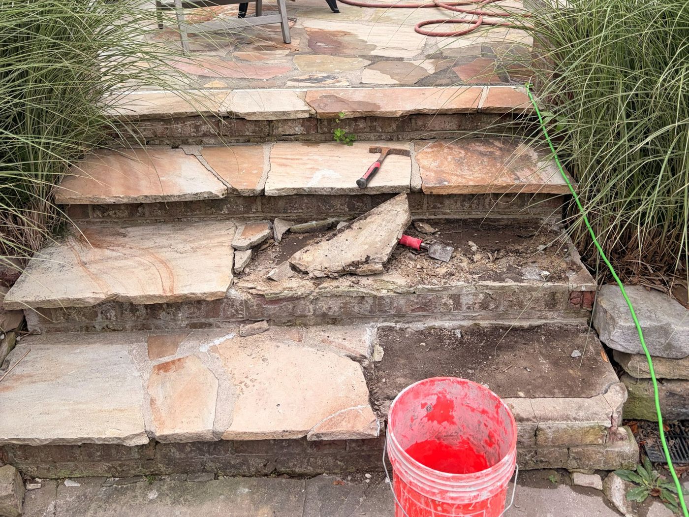 Before: flagstone steps leading up to a patio, with the middle step torn out and broken stone and a bucket in front