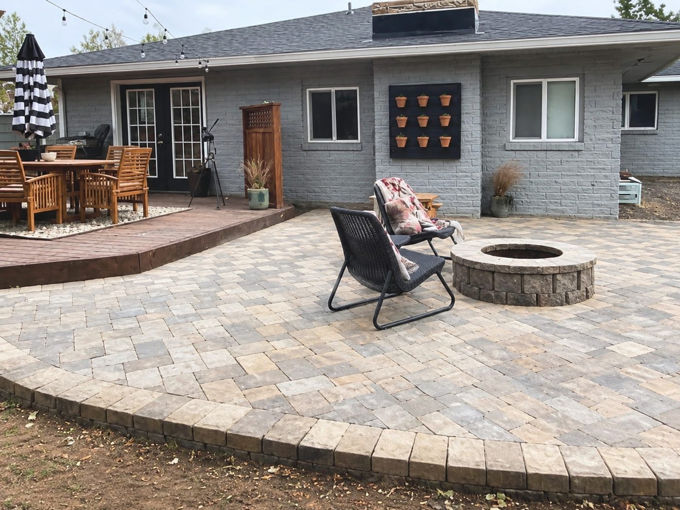 After: a finished paver patio with a curved border and stone fire pit, next to the wood deck behind the home